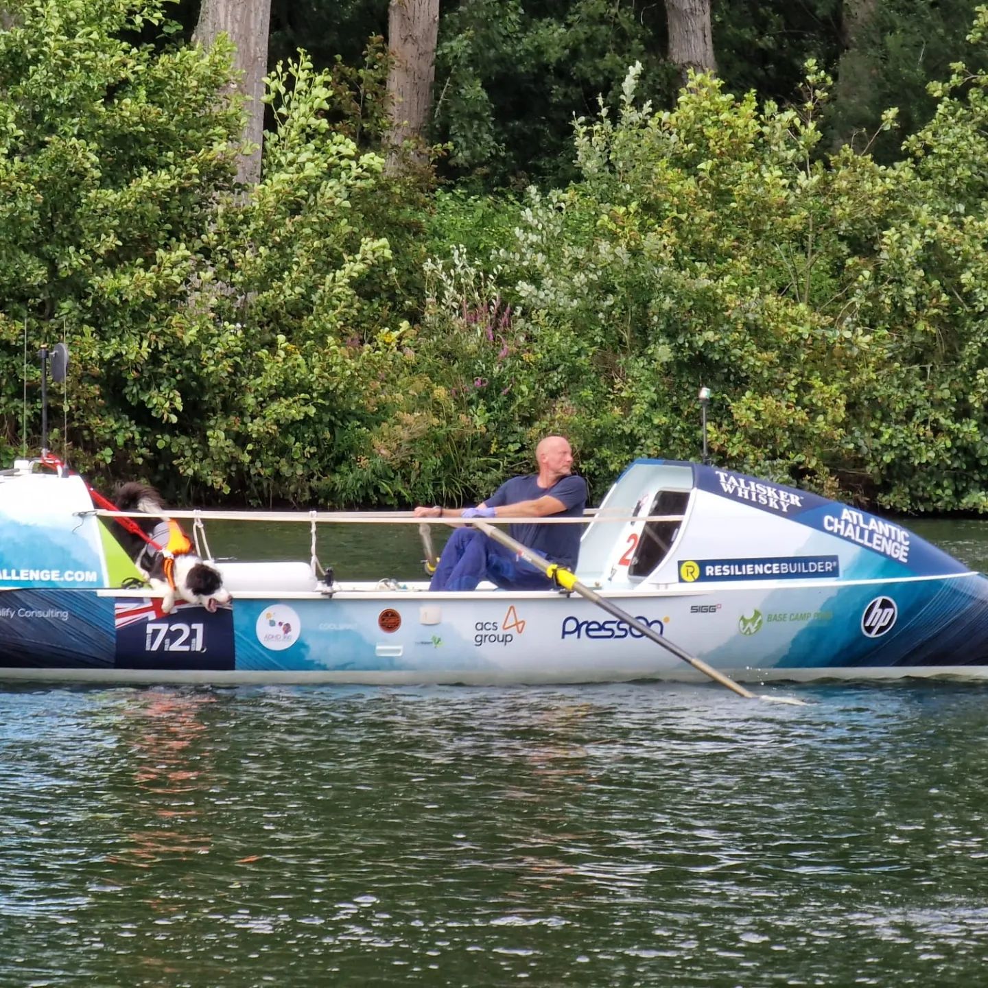 Man rows in a rowing boat on a river with a dog.