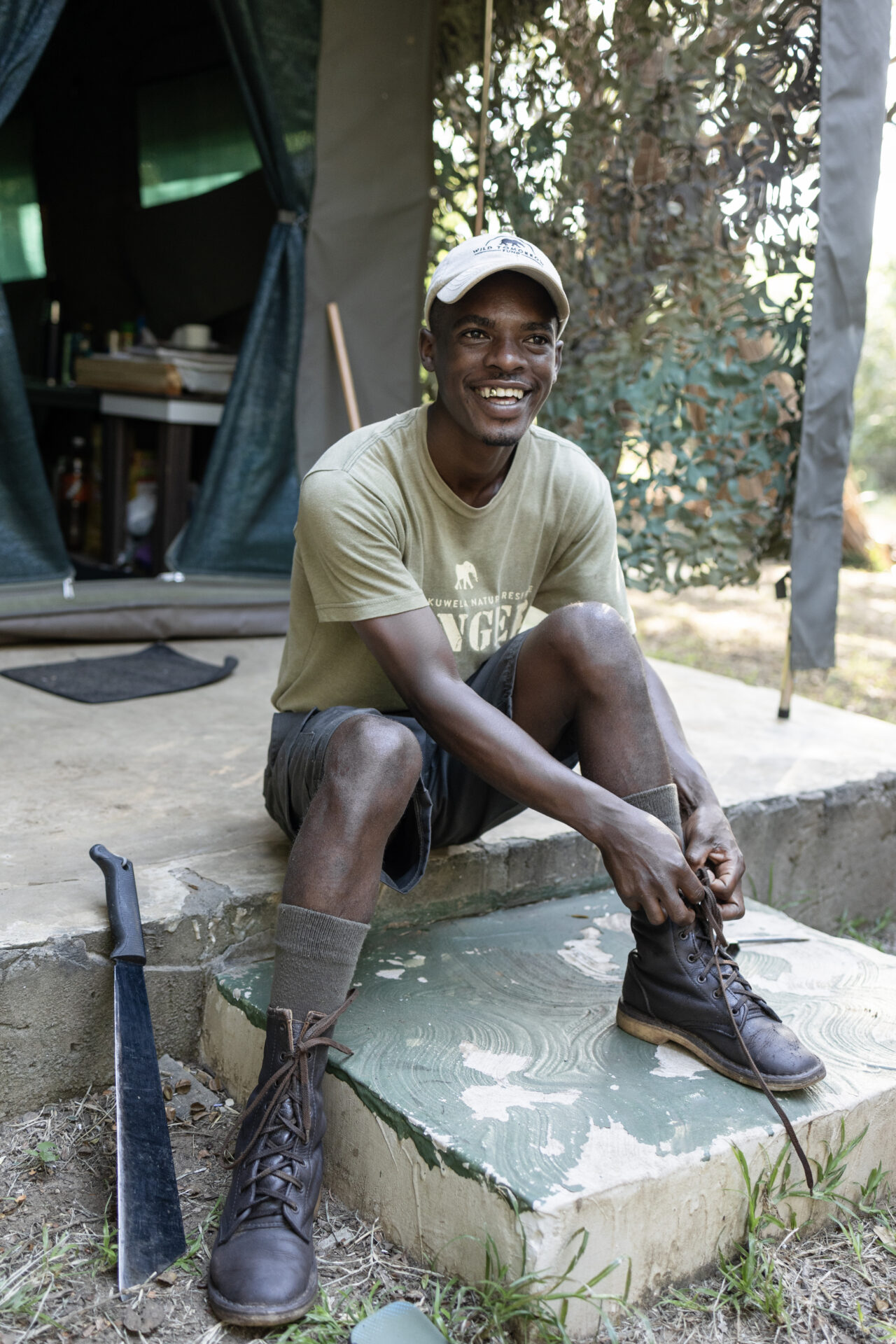 Ranger Zamani sits on the steps of the ranger hut to tie his boot laces