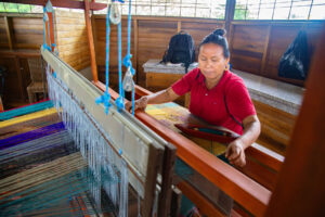 Woman using a loom, weaving multicoloured wool.