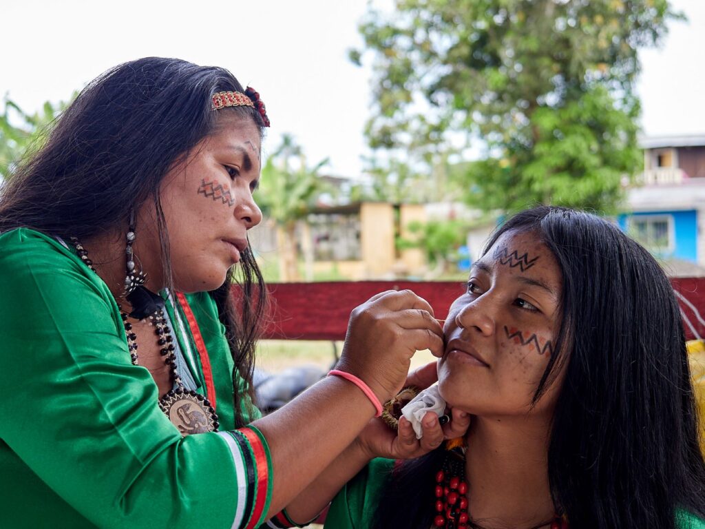 Two Indigenous women face painting in advance of an Indigenous celebration