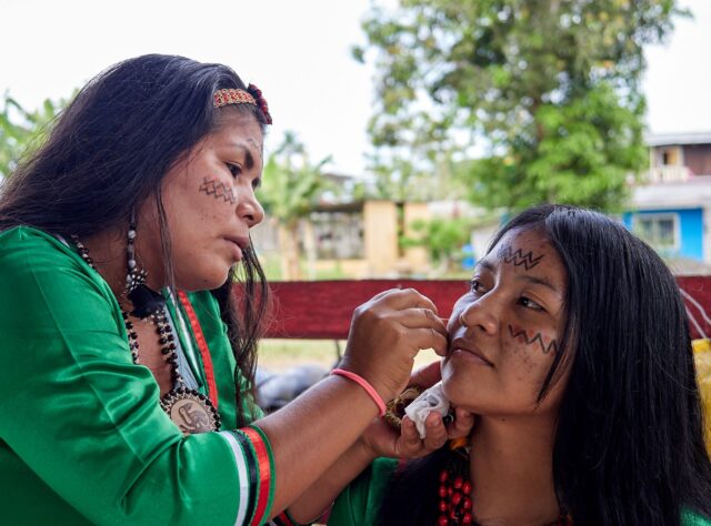 Two Indigenous women face painting in advance of an Indigenous celebration