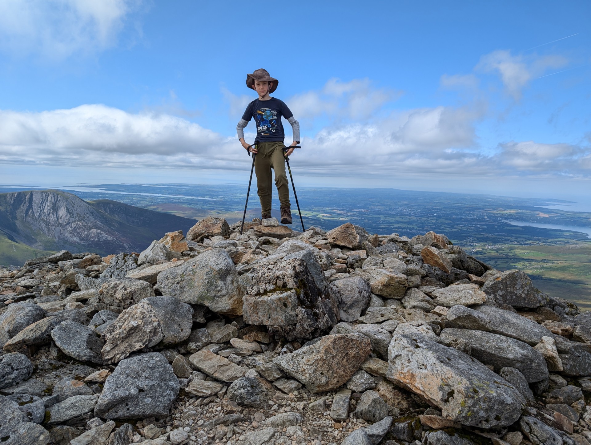 Jack standing on rocks at top of a mountain with blue sky and view of landscape behind him 