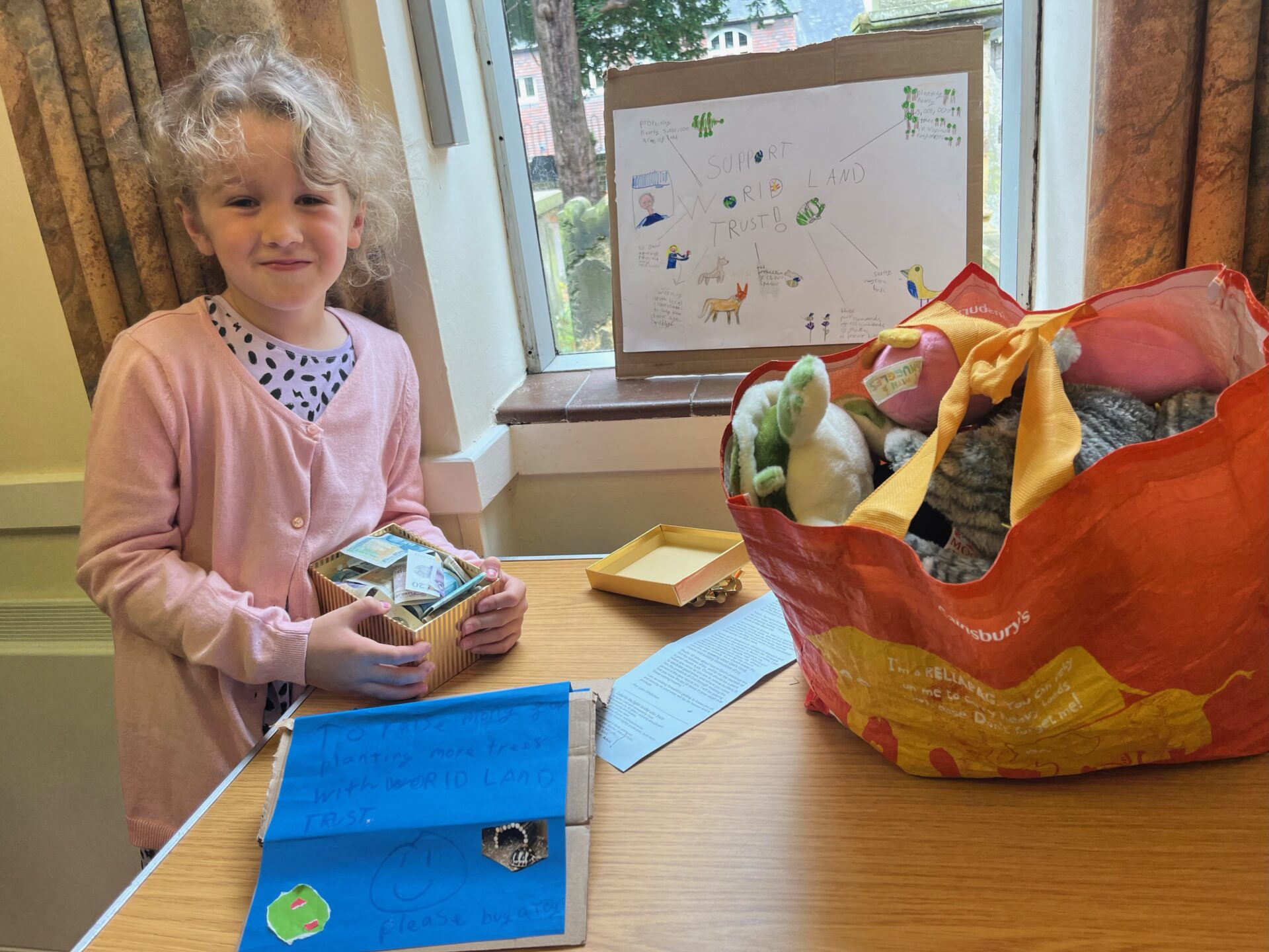 Mia Margo standing at her stall selling cuddly toys, with a poster about World Land Trusts's work