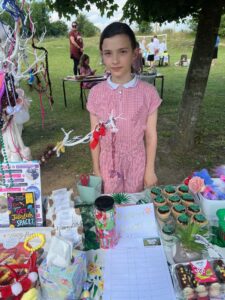 Lillianna standing at her stall, selling cakes, crochet and toys