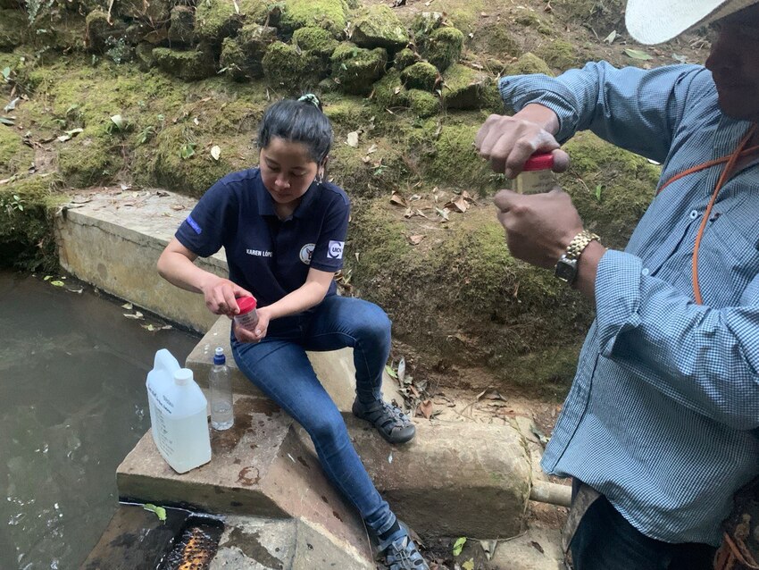 Woman and man taking water samples of water source in Honduras cloud forest. 