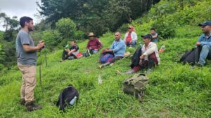People sitting in grass listening to forest ranger speak.