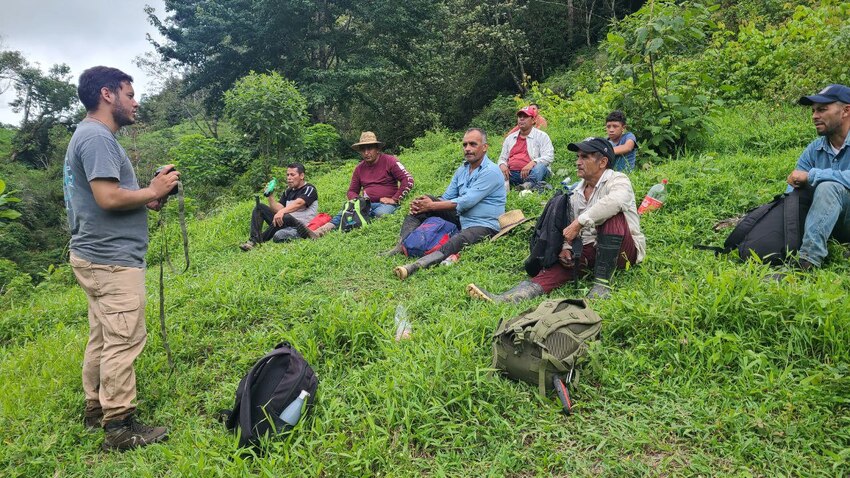 People sitting in grass listening to forest ranger speak. 