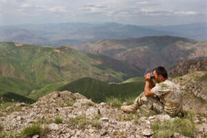 ranger with binoculars sitting on rocks overlooking the landscape of Armenia.