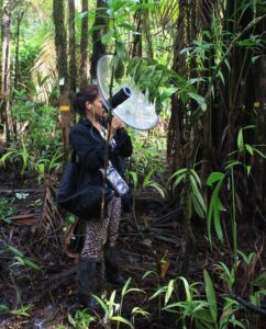 Paula Caycedo stands in a field with a specialised microphone to pick up bird song.