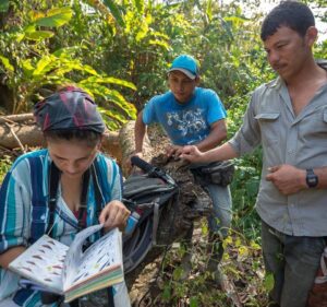 Paula Caycedo thumbs through a bird book with two colleagues in the field.